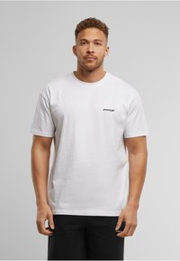White cotton T-shirt with short sleeves, crew neck, and a small black logo on the left chest area. Paired with black shorts.