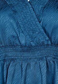 Robe bleue en tissu lisse, avec un corsage texturé en forme de croix, une taille froncée et un motif subtil de rayures de tigre.