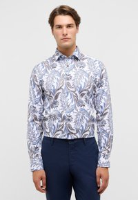 Witte blouse met een blauw en bruin bloemenpatroon, flexibele stof, lange mouwen en een button-down kraag. Gemaakt met marineblauwe broek.