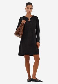 Černé sametové šaty s dlouhými rukávy, kulatým výstřihem a stříbrnými knoflíkovými detaily. V kombinaci s leopardím vzorem na kabelce přes rameno a plochými botami.