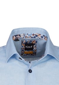 Camicia azzurra chiara con taglio moderno, dotata di colletto interno a motivo floreale e un bottone nero sul davanti. Etichetta visibile all'interno.