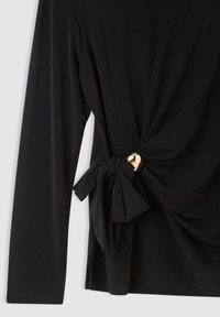 Maglietta nera a maniche lunghe con dettaglio a nodo attorcigliato sul lato, caratterizzata da un accento circolare dorato. Realizzata in tessuto morbido e elasticizzato.