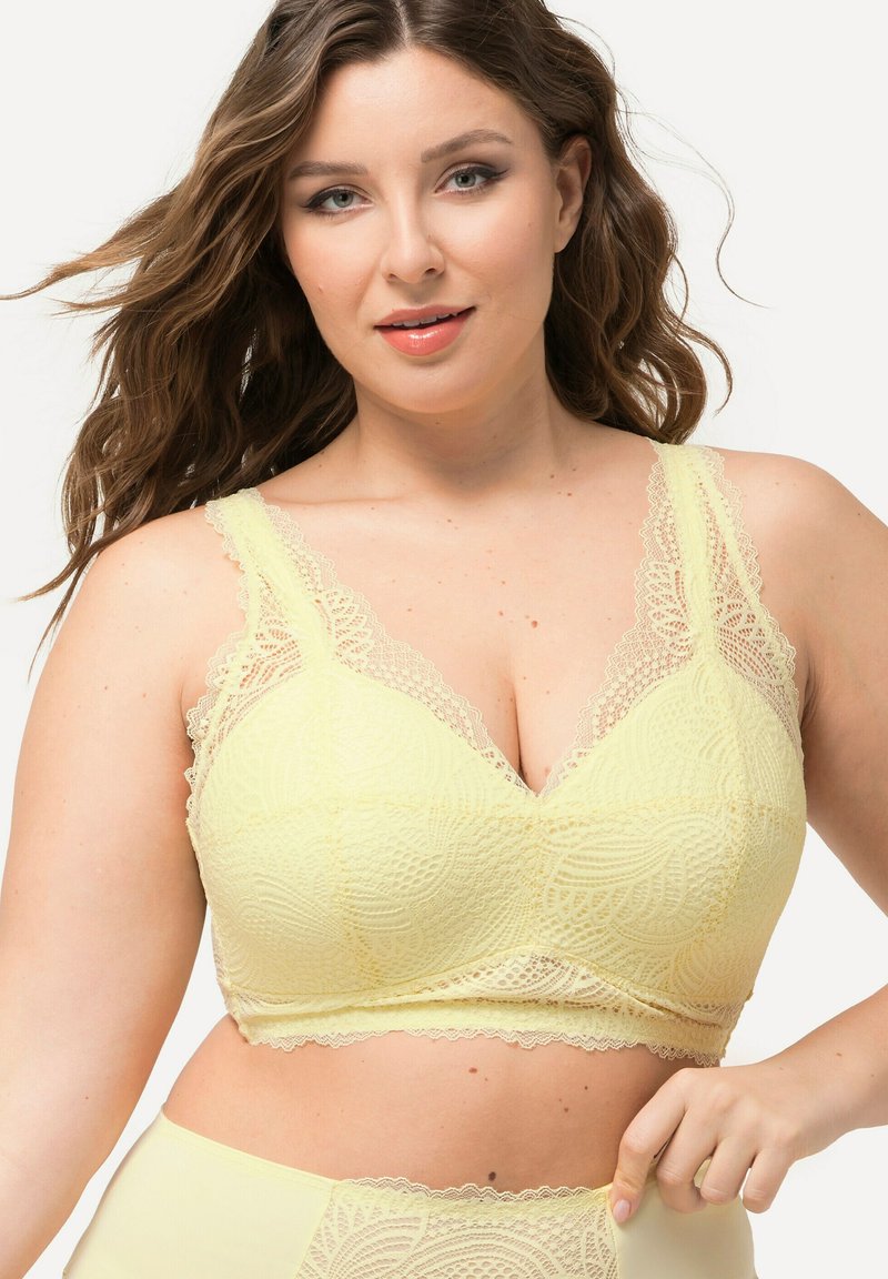 Keltainen pitsinen bralette, jossa on V-pääntie, sahalaitaiset hihnat ja kukkakuvioita. Pehmeä rakenne herkällä brodeeratulla desigillä.