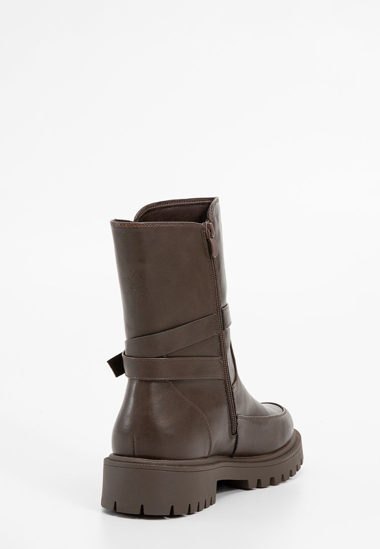 Botte en cuir marron à hauteur de genou avec une semelle épaisse, fermeture éclair latérale et sangle décorative. Texture lisse avec un minimum de détails.