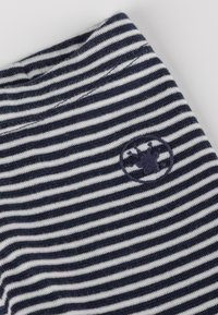 Tessuto a righe blu navy e bianco con una texture morbida; presenta un logo circolare blu navy con un motivo che somiglia a una corona sul bordo.