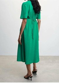 Robe midi verte avec de courtes manches ballons, une taille cintrée et un détail à nouer à l'arrière. Tissu lisse avec un léger éclat. Sandales à talons noires.