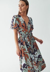 Robe florale multicolore avec un décolleté en V profond, taille élastique, manches courtes et un ourlet fluide. Fabriquée en tissu léger et texturé.