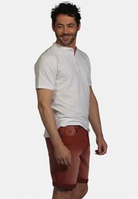 Chemise blanche à manches courtes avec col, associée à un short en denim rouge avec des revers et un subtil logo "W" sur la poche arrière.
