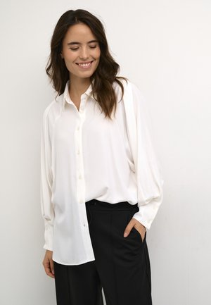 Witte blouse met lange, licht gepofte mouwen en een gladde textuur, gecombineerd met zwarte, op maat gemaakte broek. Minimalistisch ontwerp.
