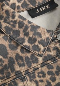 Cuello de chaqueta de mezclilla con estampado de leopardo, que presenta patrones en negro y marrón, costuras grises y una etiqueta de marca con acentos metálicos.