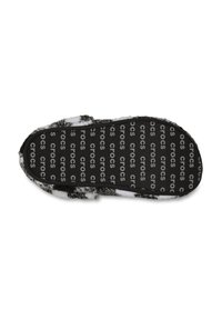 Suola in gomma nera con logo "crocs" in rilievo, circondata da un morbido rivestimento in pelliccia bianca e grigia, che offre un contrasto tattile.