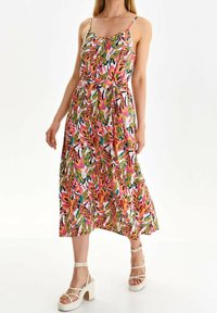 Kukallinen maksimekko, jossa on kirkas monivärinen kuvio, kevyttä kangasta, ohuet hihnat ja solmittava vyö vyötäröllä. Yhdistettynä paksuihin valkoisiin korkokenkiin.