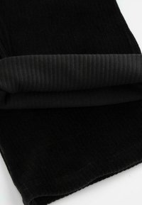 Czarna tkanina o miękkiej, prążkowanej fakturze, prezentująca złożony brzeg. Materiał wydaje się przytulny i gruby, idealny do odzieży lub akcesoriów.