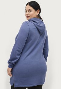 Sudadera con capucha en suave tejido azul texturizado. Presenta mangas largas, aberturas laterales y un ajuste relajado, que llega hasta la mitad del muslo.