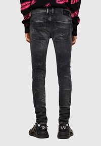 Vaqueros negros de denim ajustados con detalles descoloridos, dos bolsillos traseros y una etiqueta de marca en la cintura, combinados con zapatos deportivos negros.