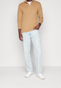 Maglione beige con zip e texture a coste, abbinato a jeans azzurri a gamba diritta e sneakers bianche. Outfit semplice e casual.