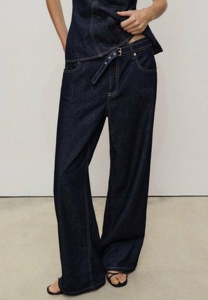 Dark blue denim wide-leg pants with a high waist, contrasting stitching, a belt loop, and pockets, paired with black strappy sandals.