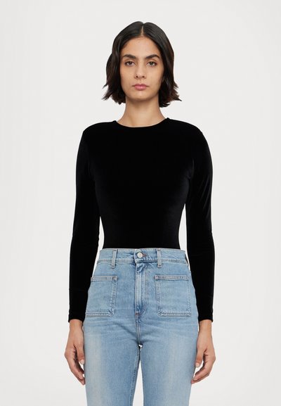 Svart langermet bodysuit laget av myk fløyel, kombinert med høy midje lys blå jeans med to frontlommer og knappelukking.