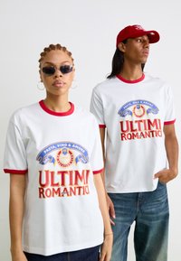 Witte T-shirts met rode trim die een kleurrijke grafische tekst "ULTIMI ROMANTICI" en logo's tonen. Draag door twee modellen, waarvan één een zonnebril draagt.