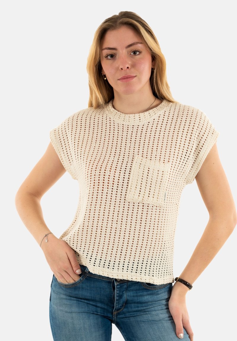 Crème-kleurige gebreide top met korte mouwen en een losse pasvorm, met een gestructureerde open weving en een voorzak. Gecombineerd met blauwe denim jeans.