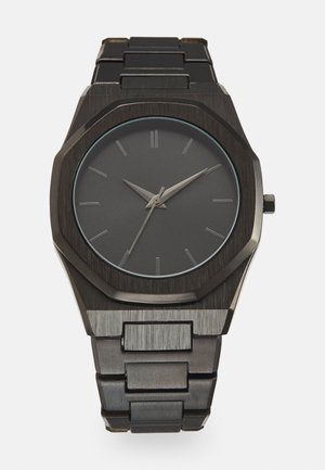 Montre en acier inoxydable noir avec un cadran rond noir mat. Présente des aiguilles des heures et des minutes argentées, des repères de 12 heures et un design de boîtier octogonal.