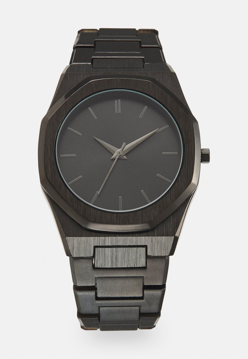 Montre en acier inoxydable noir avec un cadran rond noir mat. Présente des aiguilles des heures et des minutes argentées, des repères de 12 heures et un design de boîtier octogonal.