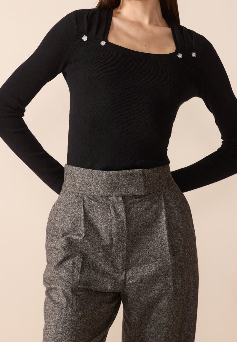 Czarny prążkowany top z długim rękawem i kwadratowym dekoltem, ozdobiony dwoma srebrnymi ćwiekami, zestawiony z szarymi, teksturowanymi spodniami z wysokim stanem z plisami.