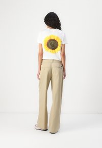 T-shirt blanc avec un grand imprimé de tournesol au dos, associé à un pantalon large beige clair. Texture subtile et coupe décontractée.