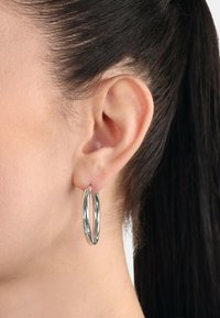 Pendientes de aro de plata con un diseño retorcido, que presentan una superficie lisa y reflectante. Sujetos al lóbulo de la oreja, exhiben un acabado pulido.