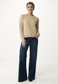 Beige gestrickter Pullover mit rundem Halsausschnitt und gerippten Bündchen, kombiniert mit hoch taillierten, weit geschnittenen dunkelblauen Jeans. Glatte Textur, lässige Passform.