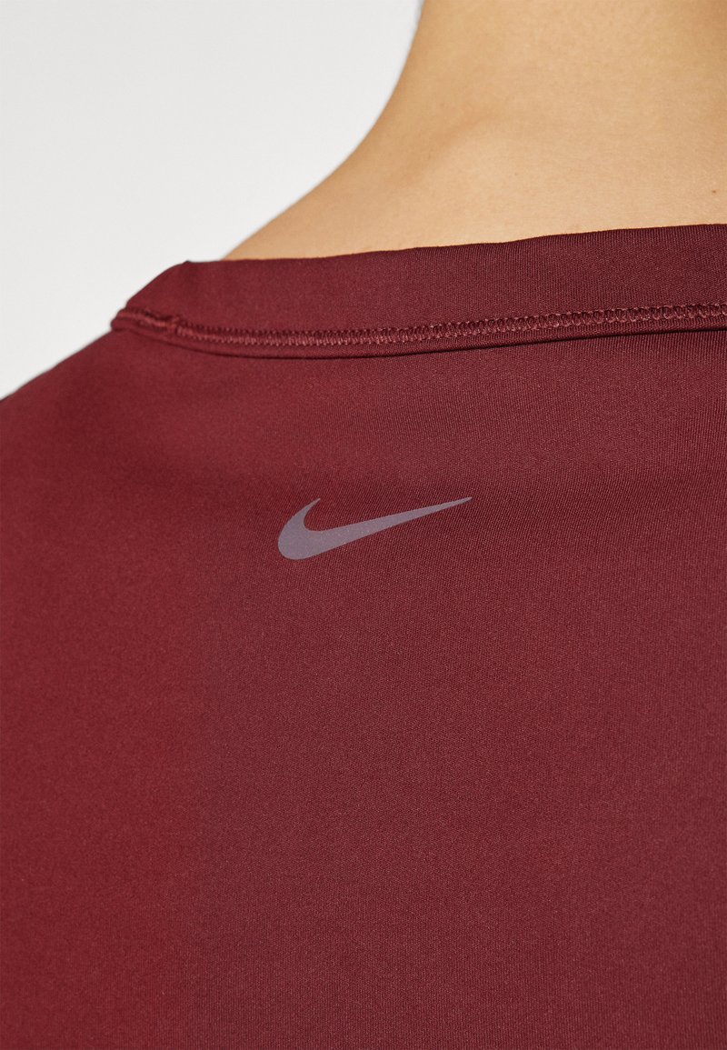 Maglietta sportiva color bordeaux con una texture liscia, presenta un sottile logo Nike grigio sul retro vicino al collo. I dettagli delle cuciture sono visibili.