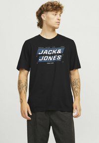 Sort t-shirt med et blåt og hvidt "JACK & JONES" grafisk print i midten. Korte ærmer og rund hals. Blødt bomuldsmateriale.