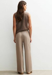 Un haut sans manches marron en tissu doux associé à un pantalon large beige clair, doté d'une taille élastique et d'une texture lisse.