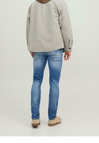 Jasnoszary sweter z okrągłym dekoltem, luźnym krojem i opuszczonymi ramionami; zestawiony z jasnoniebieskimi dżinsami i beżowymi butami.