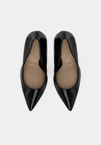Des escarpins en cuir verni noir à bout pointu avec une finition lisse et brillante et une semelle intérieure beige. Présente une silhouette épurée et raffinée pour un attrait moderne.