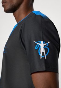 Czarny sportowy T-shirt z niebieskimi akcentami, na rękawie ma białą grafikę osoby oraz fakturowane wykończenie.