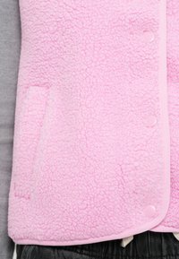 Rosa fleecevest med teksturert overflate, trykknapplukking og sidelomme. Pyntet med en ensfarget rosa kant, lagdelt over en grå topp.