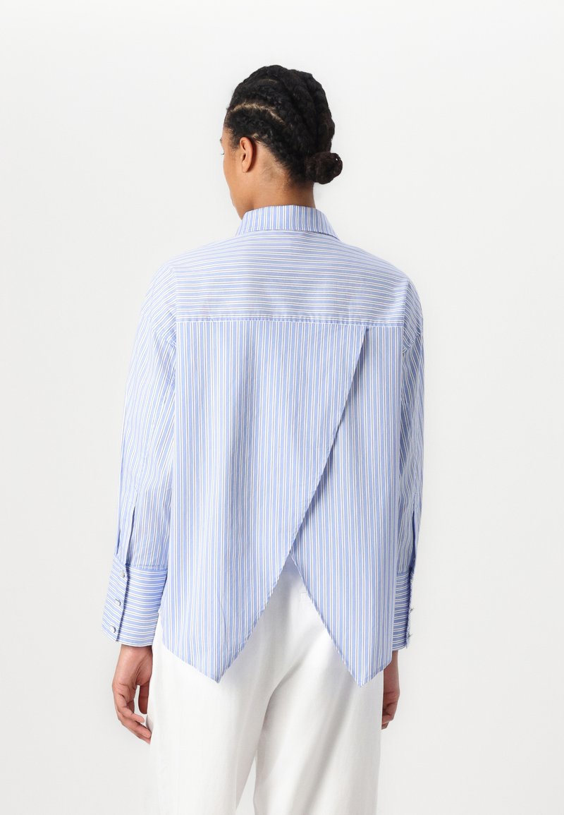 Niebieska i biała koszula w paski z wydłużonym tyłem, długimi rękawami, mankietami na guziki i klasycznym kołnierzykiem. Wykonana z lekkiego materiału.