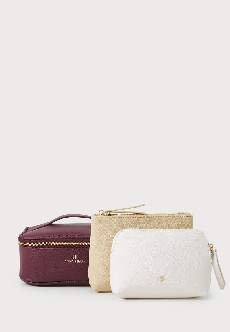 Conjunto de tres bolsas de cosméticos en burdeos, beige y blanco. Hechas de material texturizado con cremalleras doradas y detalles de marca.