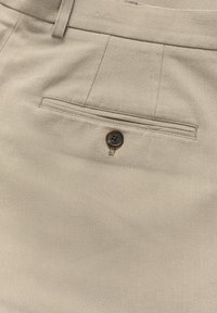 Pantaloni din țesătură bej cu pliuri în față, buzunar la spate cu un nasture maro și textură netedă.
