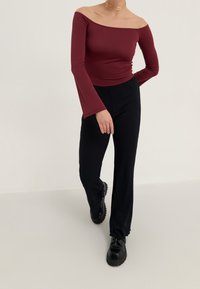 Top color bordeaux senza spalle con lunghe maniche a campana abbinato a pantaloni neri a coste e scarpe nere spesse. Texture del tessuto liscia.