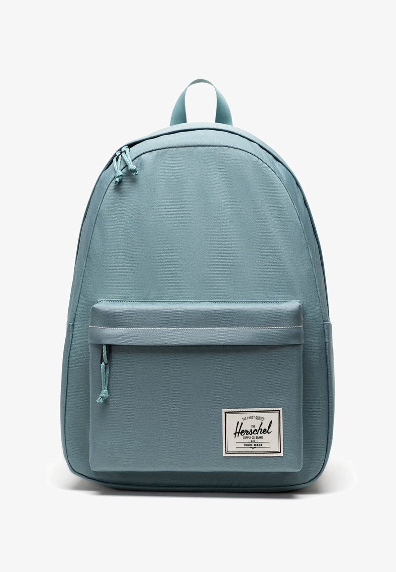 Sac à dos en tissu bleu clair à la forme arrondie, avec une poche avant zippée et une étiquette tissée. Dispose de bretelles réglables et d'une poignée supérieure.