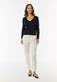 Zwarte V-hals sweater, crèmekleurige broek en zwarte ballerina's. De outfit heeft een getailleerd ontwerp met gladde texturen en geen zichtbare patronen.