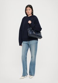 Navy oversized hoodie with a front pocket, light blue flared jeans, and cream pointed-toe heels; carrying a dark blue handbag with accents.