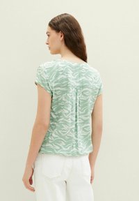 Short-sleeve blouse in light green fabric featuring a white wavy pattern, with a pleat detail at the back and a relaxed fit.
