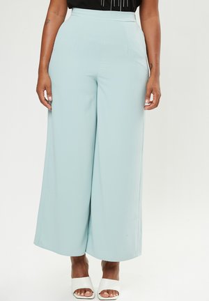 Lichtblauwe wijde broek van soepel stof, met een hoge taille en voorvouwen, gecombineerd met witte open teen hakken.