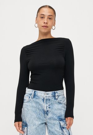 Svart langermet topp med rynkedetaljer på skuldrene, kombinert med lyseblå denim cargo-bukser med lommer og knappelukking.