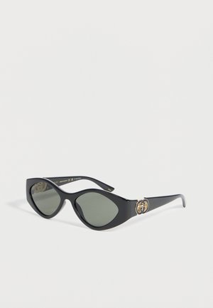 Lunettes de soleil œil de chat noires avec verres foncés et logo double G doré entrelacé sur les branches, présentées sur fond blanc.