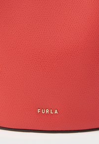 Czerwona skórzana torba o fakturowanym wykończeniu, z złotym logo „FURLA” u dołu oraz czarnymi wykończeniami na krawędziach.