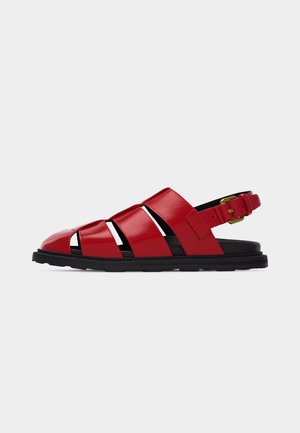 Sandale de pêcheur en cuir rouge avec semelle noire et bride réglable à boucle dorée sur fond blanc.